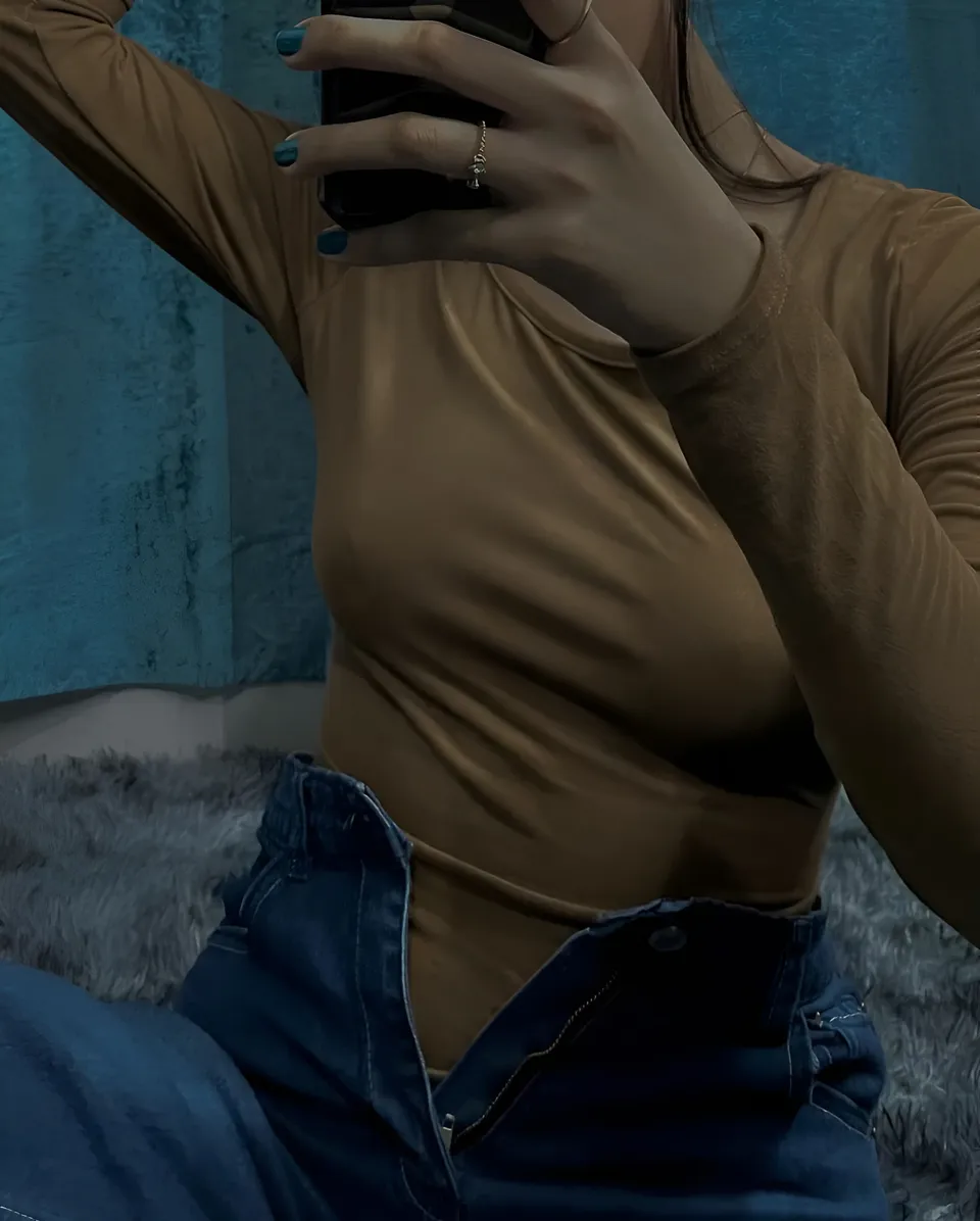 Abegail Bennett in a fitted brown top and blue jeans takes a mirror selfie