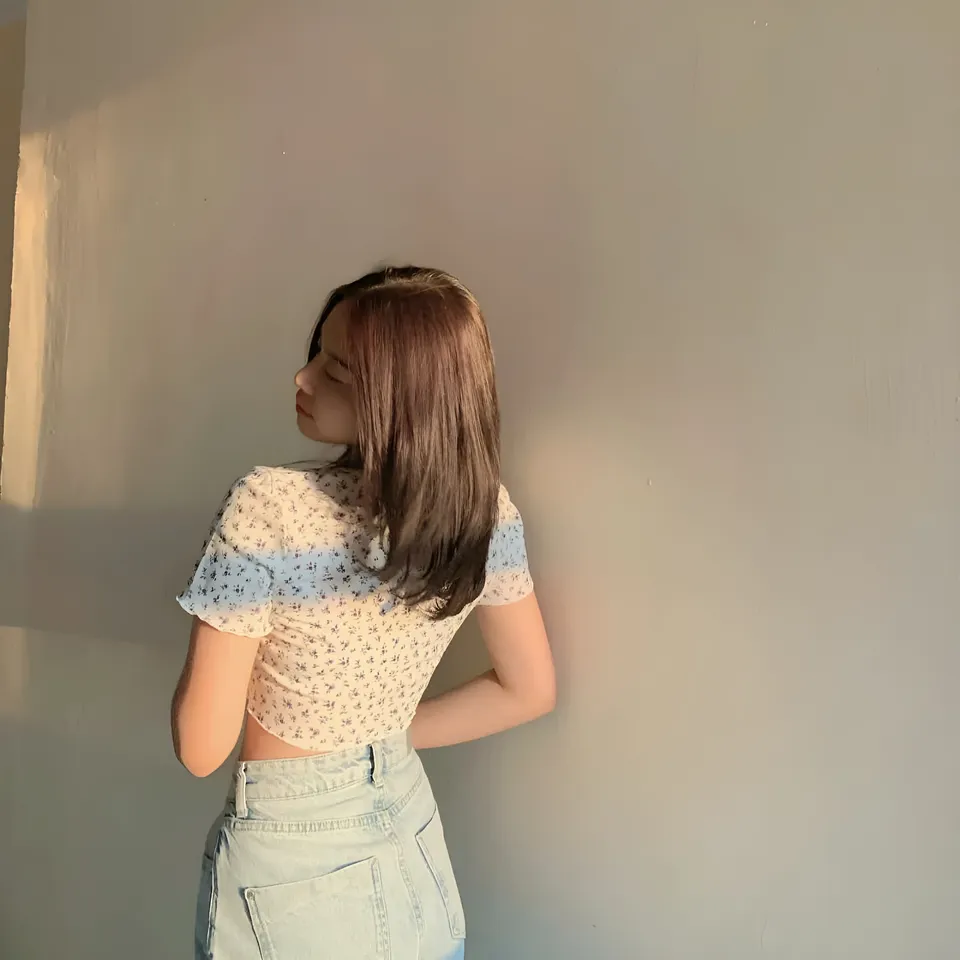 Alina Paola wearing a patterned top and jeans faces a plain wall