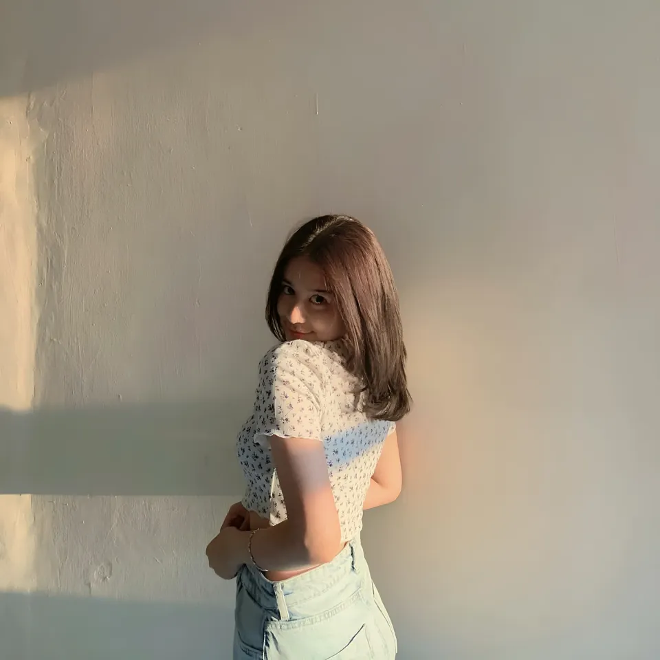 Alina Paola in patterned top standing against plain wall