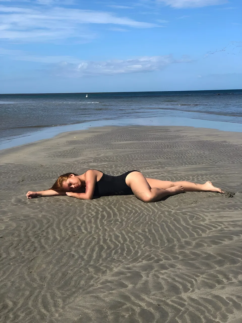 Ally Romano in black swimsuit lying on sandy beach near water