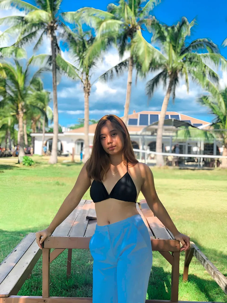 Ally Romano in black top and blue pants stands outdoors near picnic table