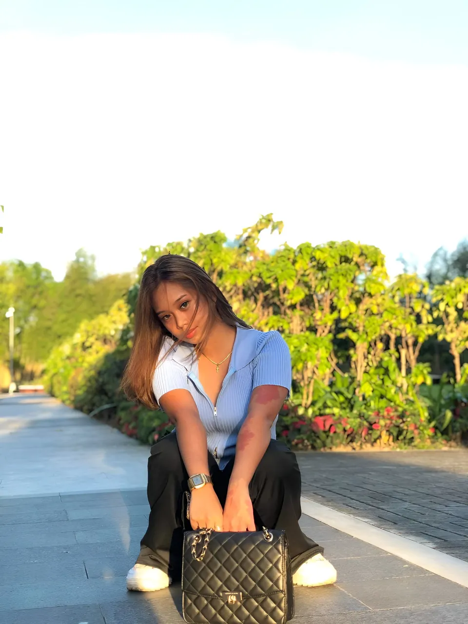 Ally Romano in blue top sits on paved path with handbag