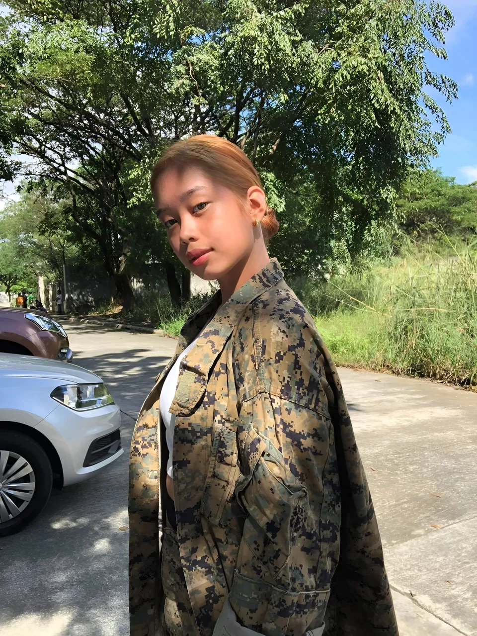 Ally Romano in camouflage jacket standing outdoors near parked cars