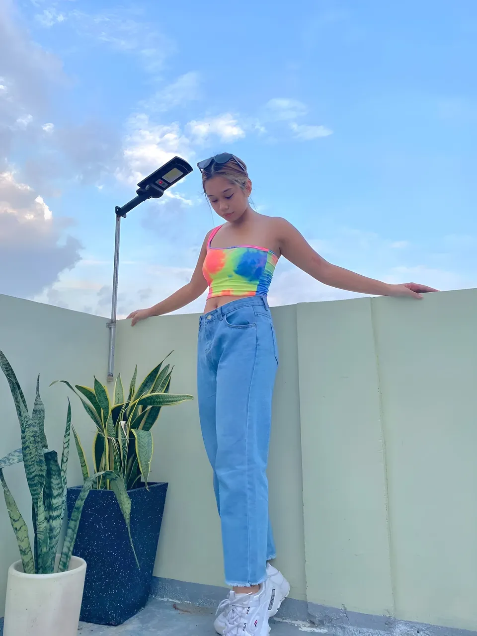 Ally Romano in colorful top and jeans standing on rooftop with plants