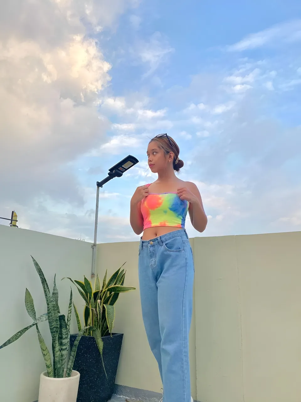 Ally Romano wearing colorful top and jeans on rooftop with plants