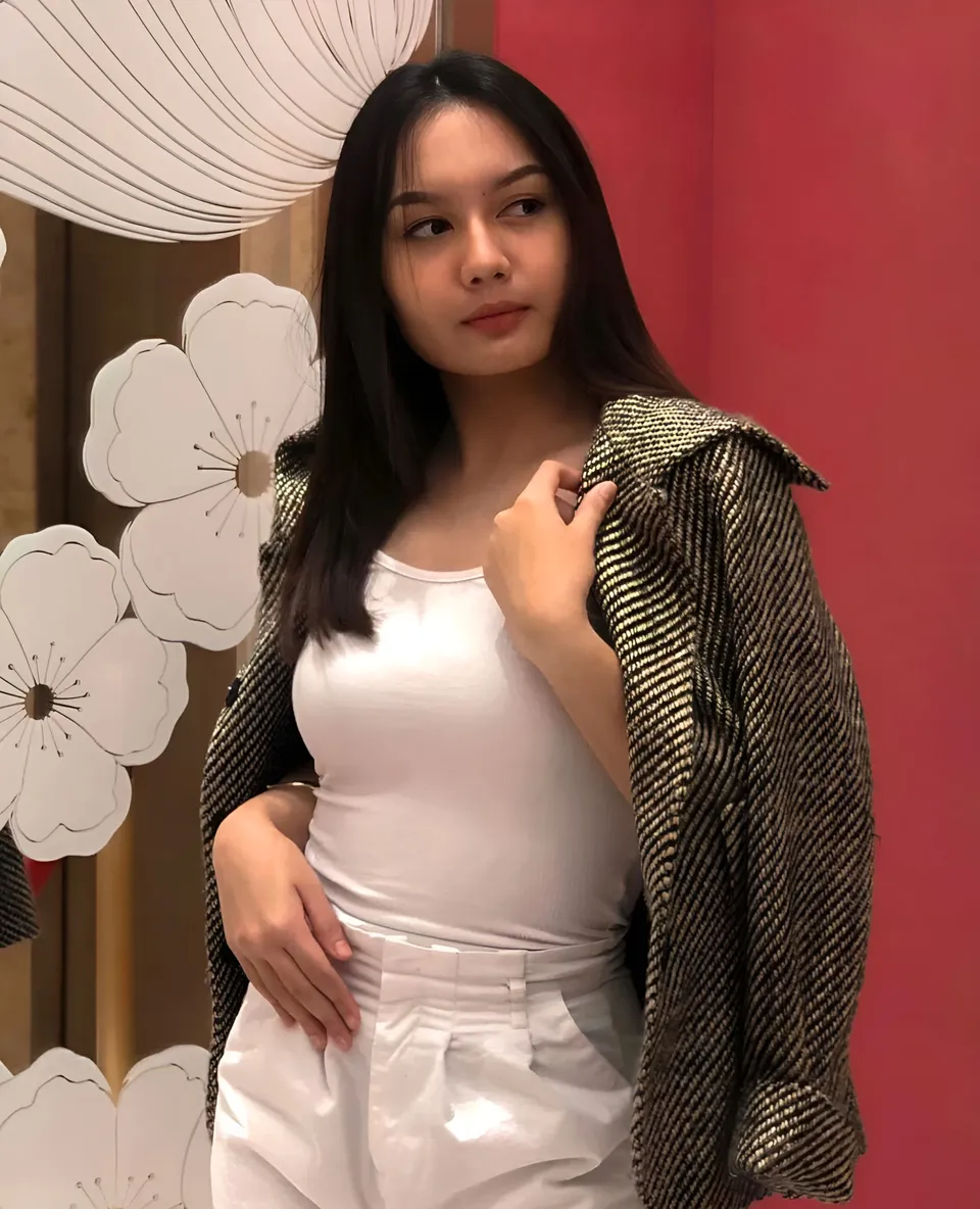 Andrea Jana Ladores wearing a white top and patterned jacket poses beside decorative flowers
