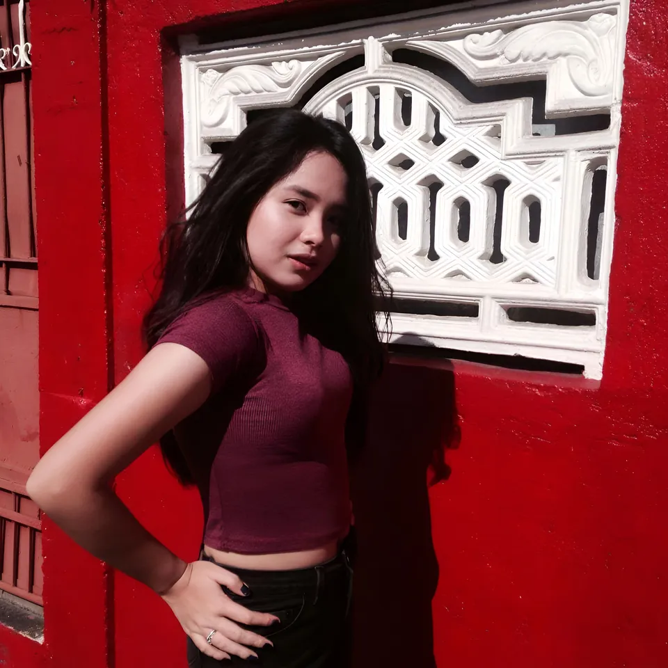 Anika Madrid in maroon top stands against red wall with white window frame