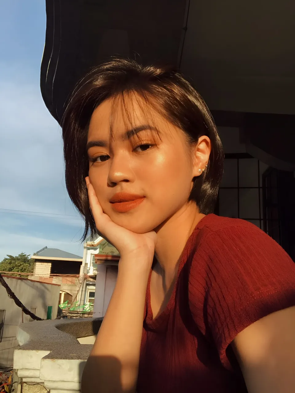 Anne Coronel in red top resting hand on cheek outdoors