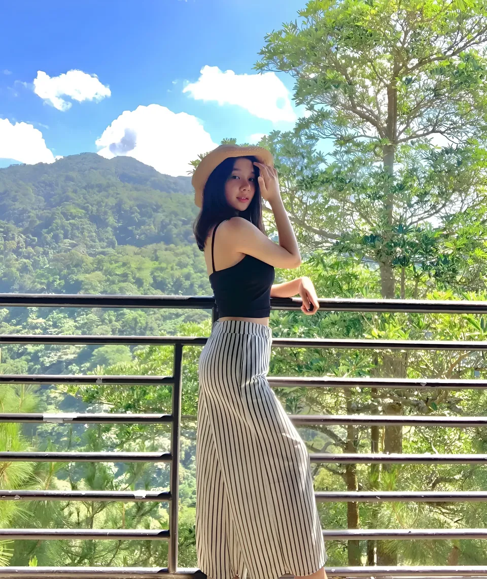 Ariane Quevedo in striped skirt and hat stands on balcony overlooking green hills