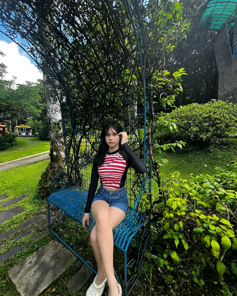 Ayesha Oprenario sitting on blue bench under green trellis
