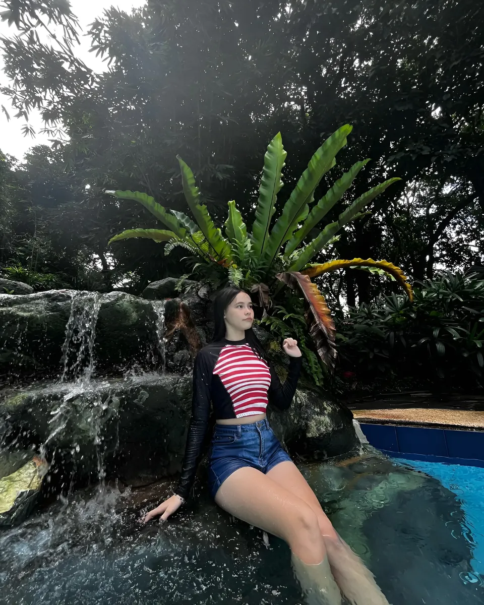 Ayesha Oprenario in striped top seated by waterfall in pool
