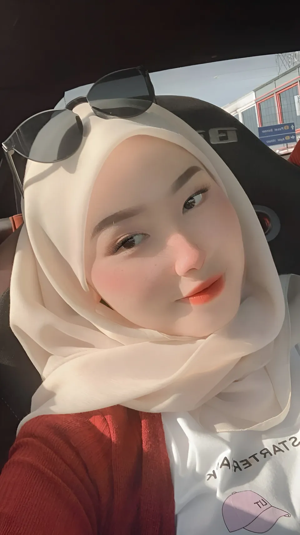 Bella Marlowe wearing a white hijab and red top takes a selfie inside a car