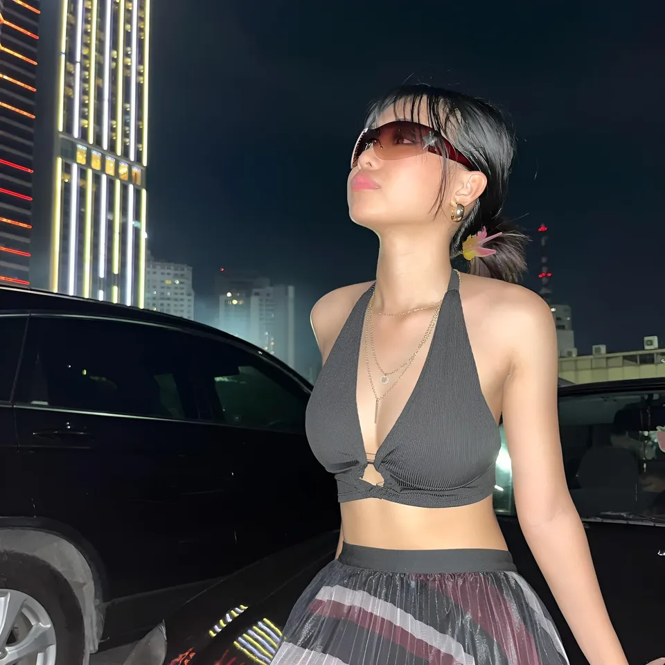 Beri Sinclair in black top and skirt stands beside black car at night