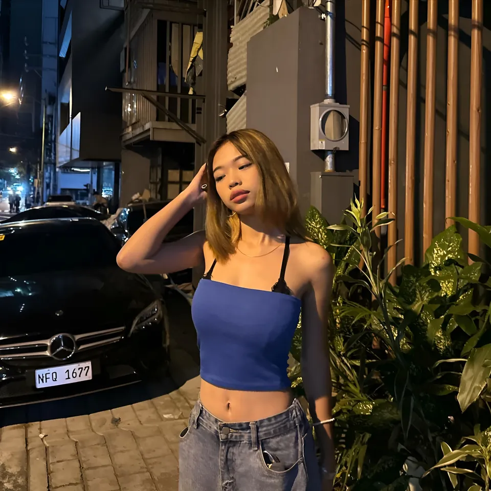 Beri Sinclair in blue crop top and jeans stands beside parked car at night
