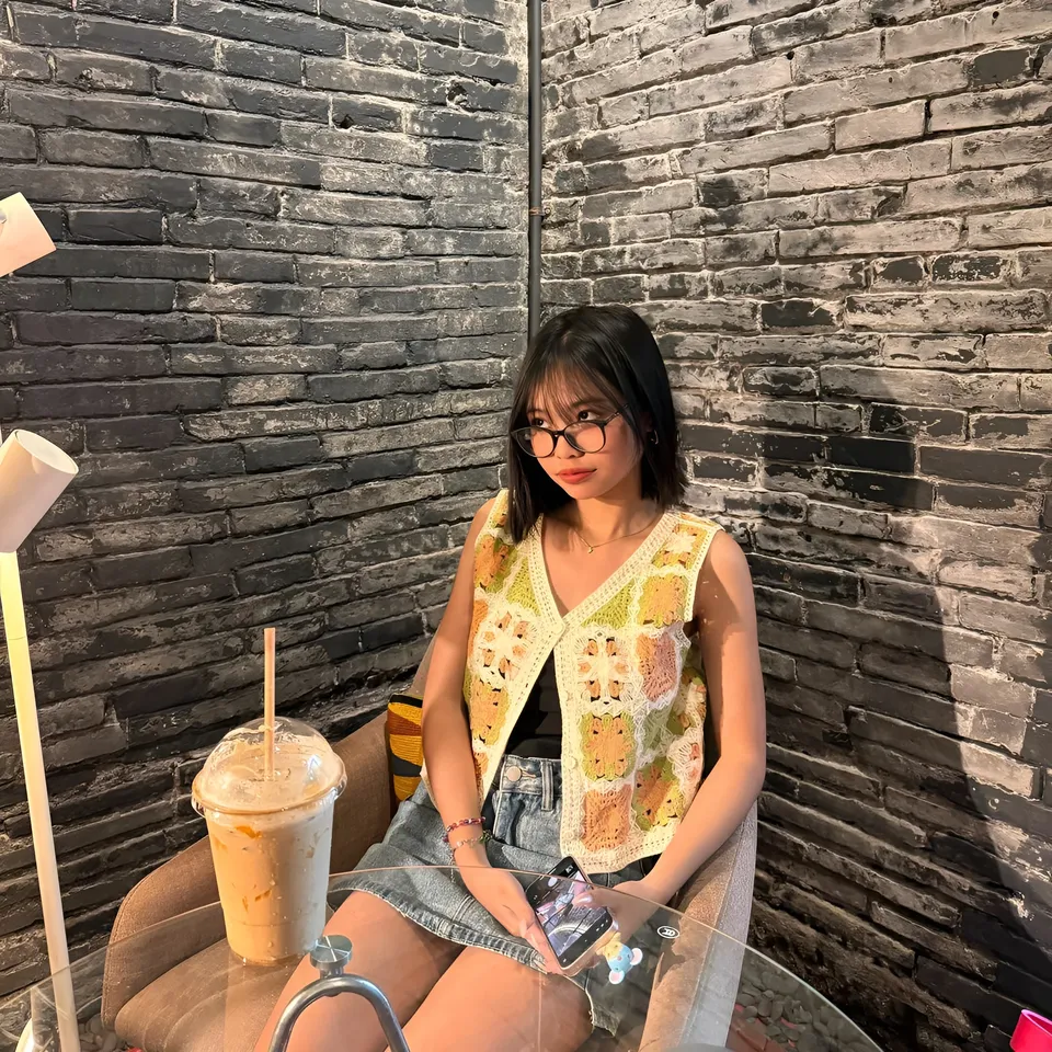 Beri Sinclair wearing crochet vest seated at table with drink