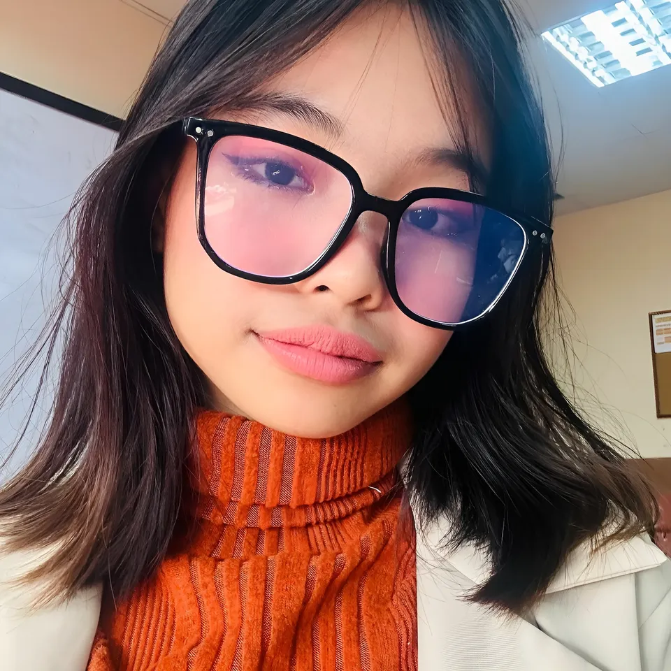 Beri Sinclair wearing glasses and orange turtleneck in indoor setting