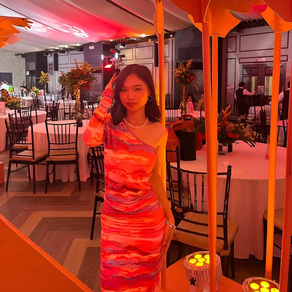 Beri Sinclair in orange dress standing in event hall with tables and chairs