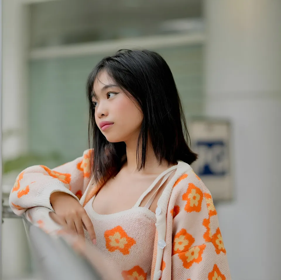 Beri Sinclair in orange floral cardigan leaning against railing indoors