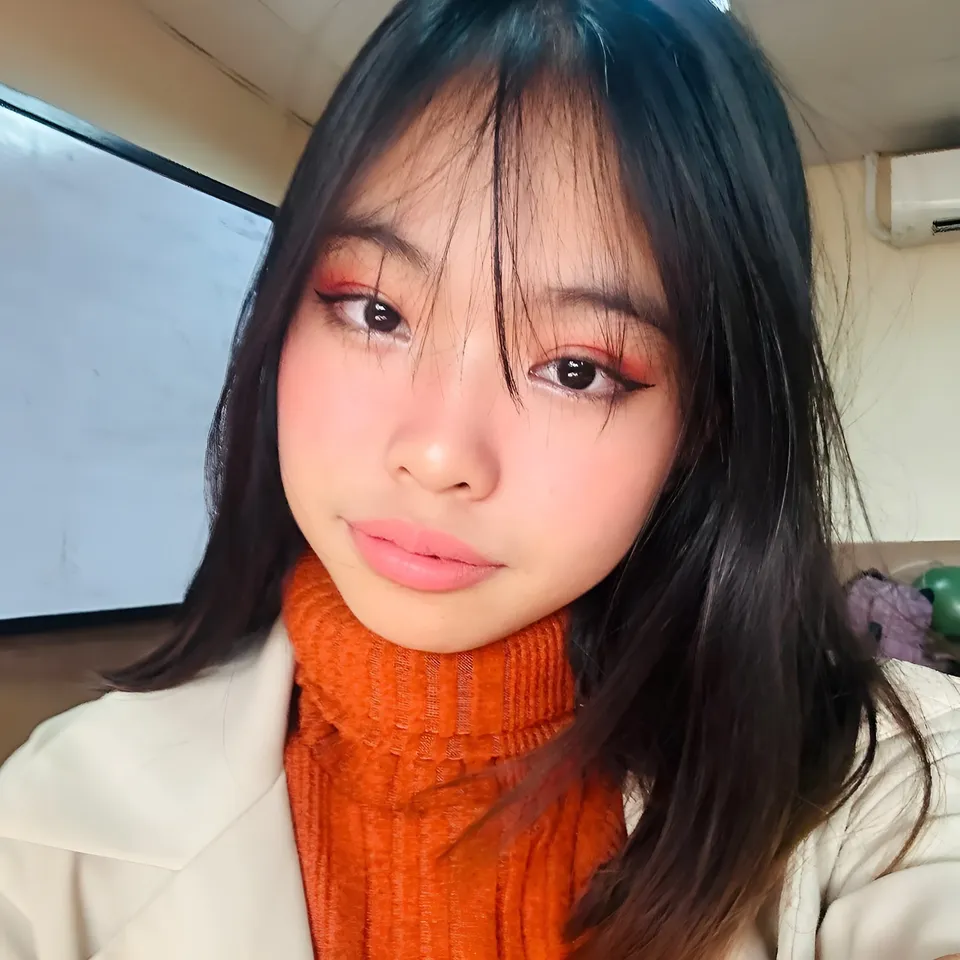 Beri Sinclair wearing orange turtleneck and white coat in indoor setting