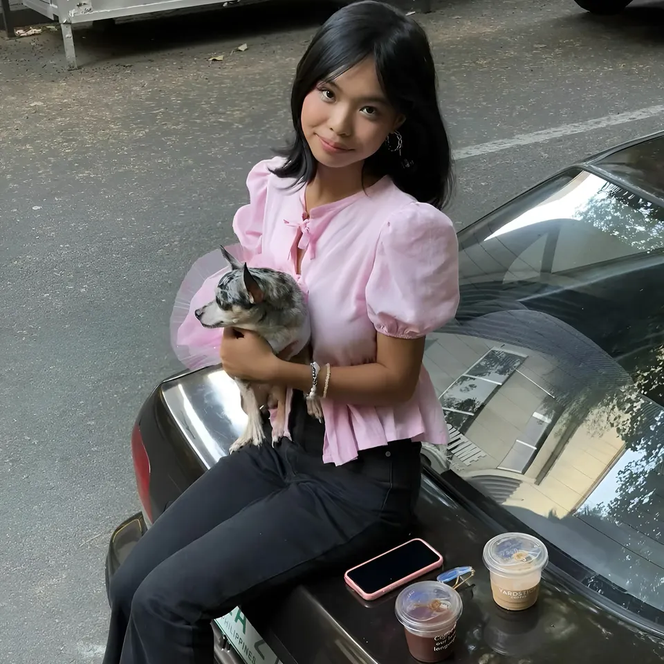 Beri Sinclair in pink top holding small dog on car hood