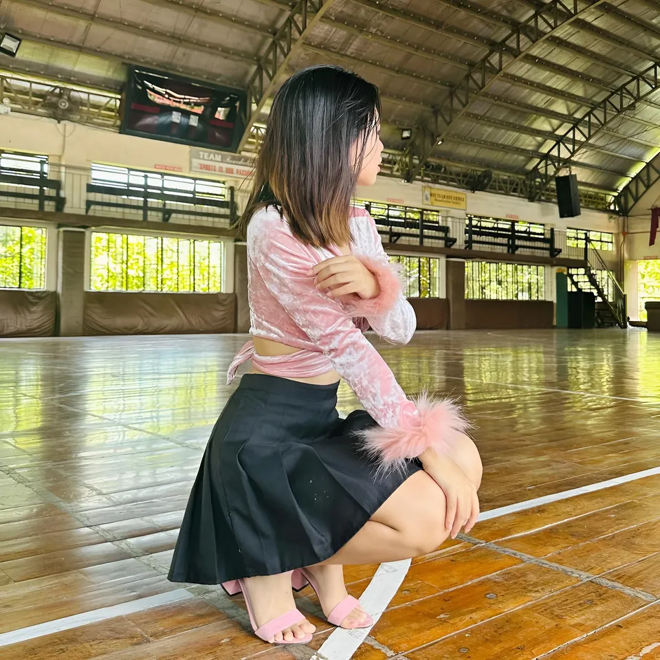Beri Sinclair in pink top and black skirt crouches on gym floor