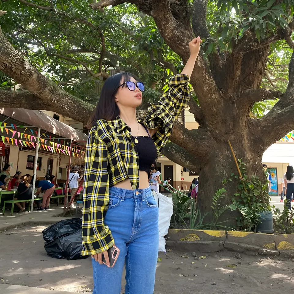 Beri Sinclair in plaid shirt stands under large tree outdoors