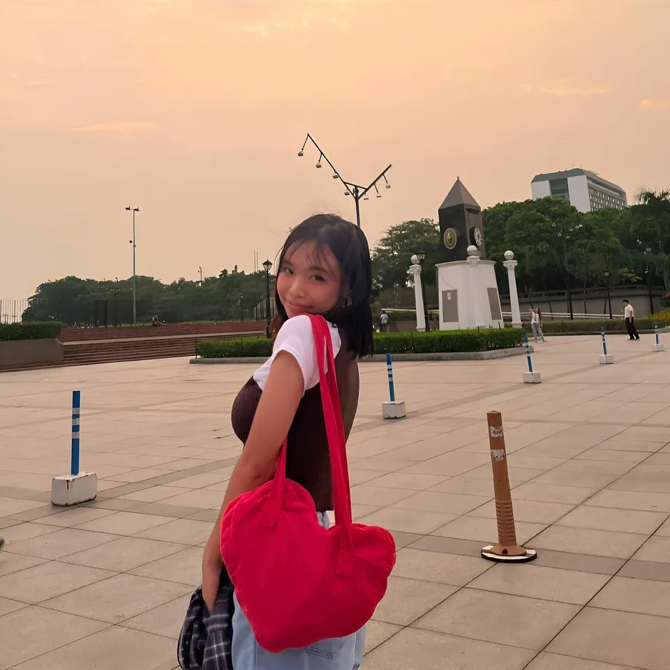 Beri Sinclair smiling while holding red bag in open paved area