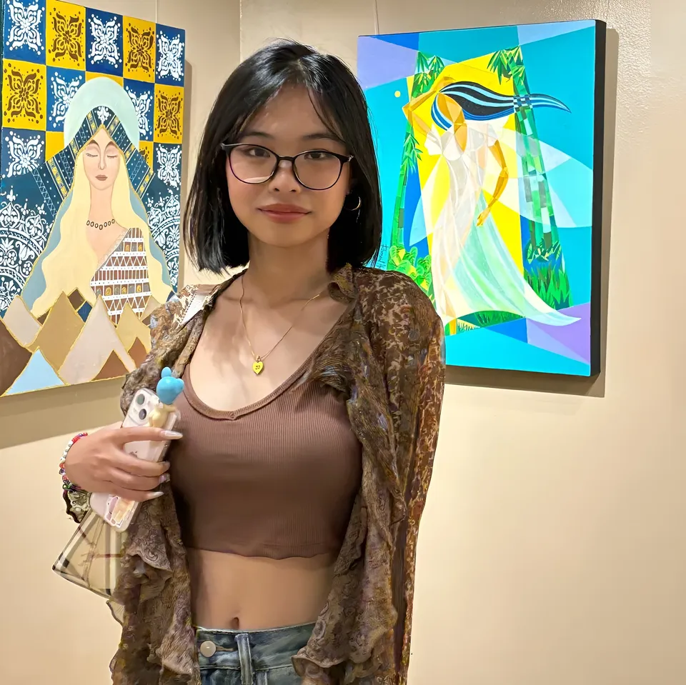 Beri Sinclair holding phone stands before two colorful paintings