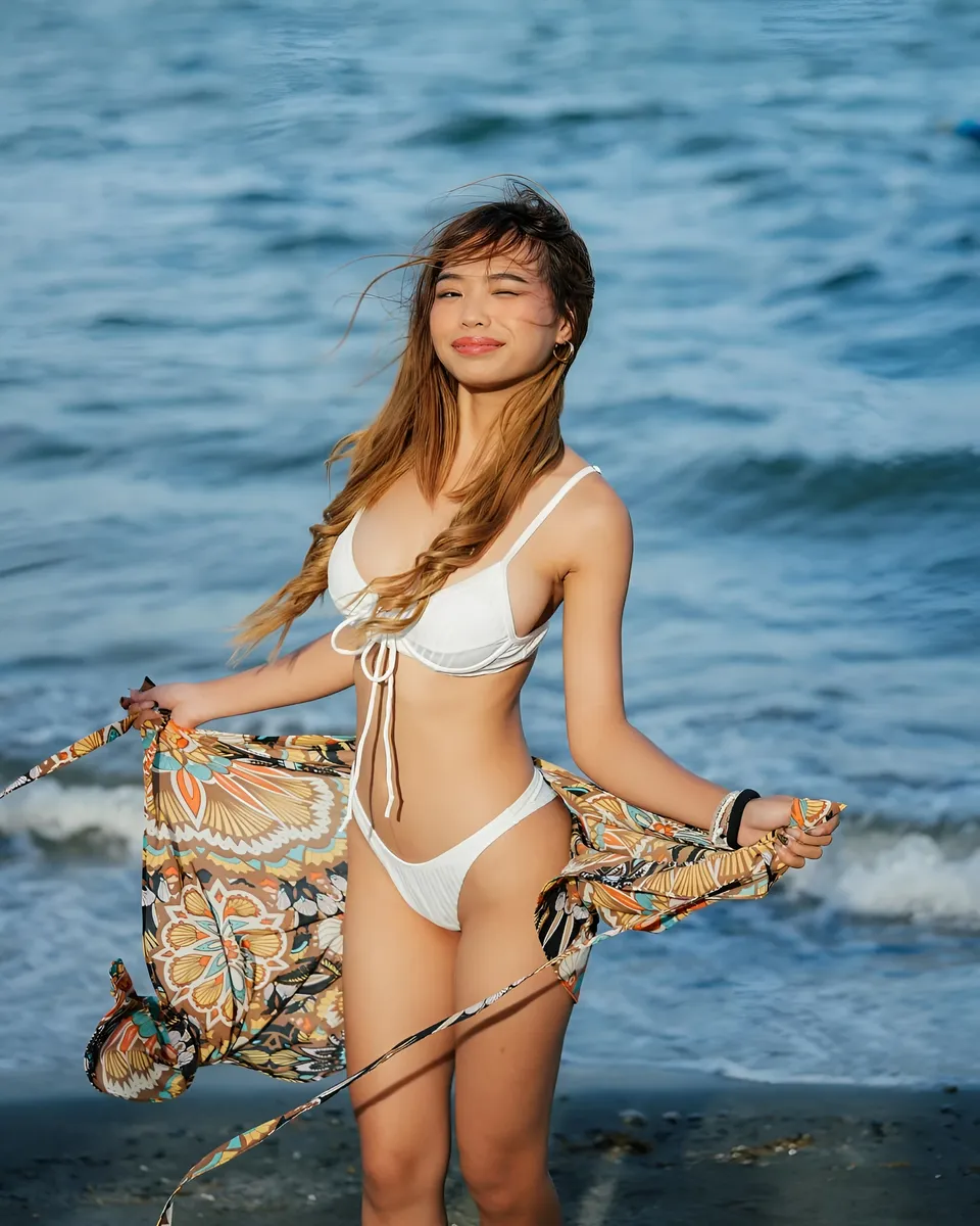 Beri Sinclair in white bikini holds patterned wrap on beach