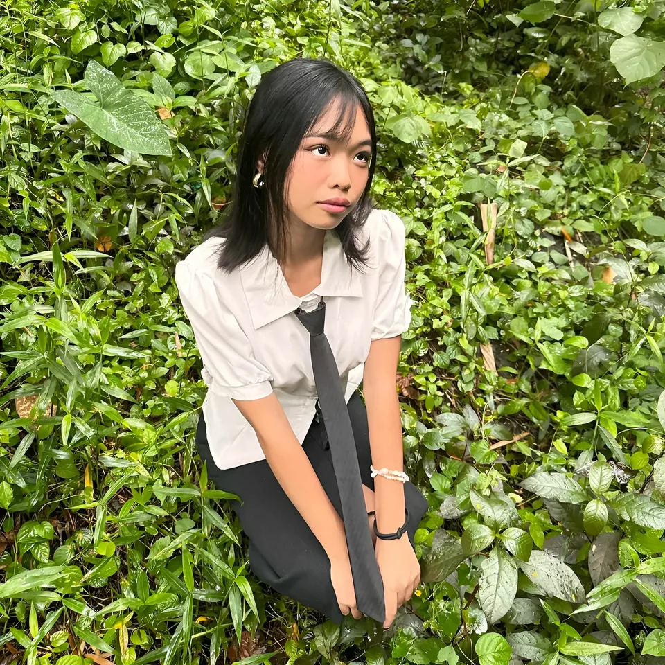 Beri Sinclair in white shirt and tie crouching in green foliage