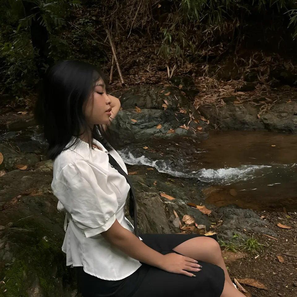Beri Sinclair in white top sits by stream in forest