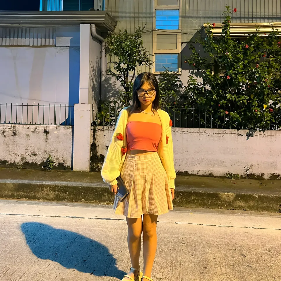 Beri Sinclair in yellow cardigan and orange top stands outdoors