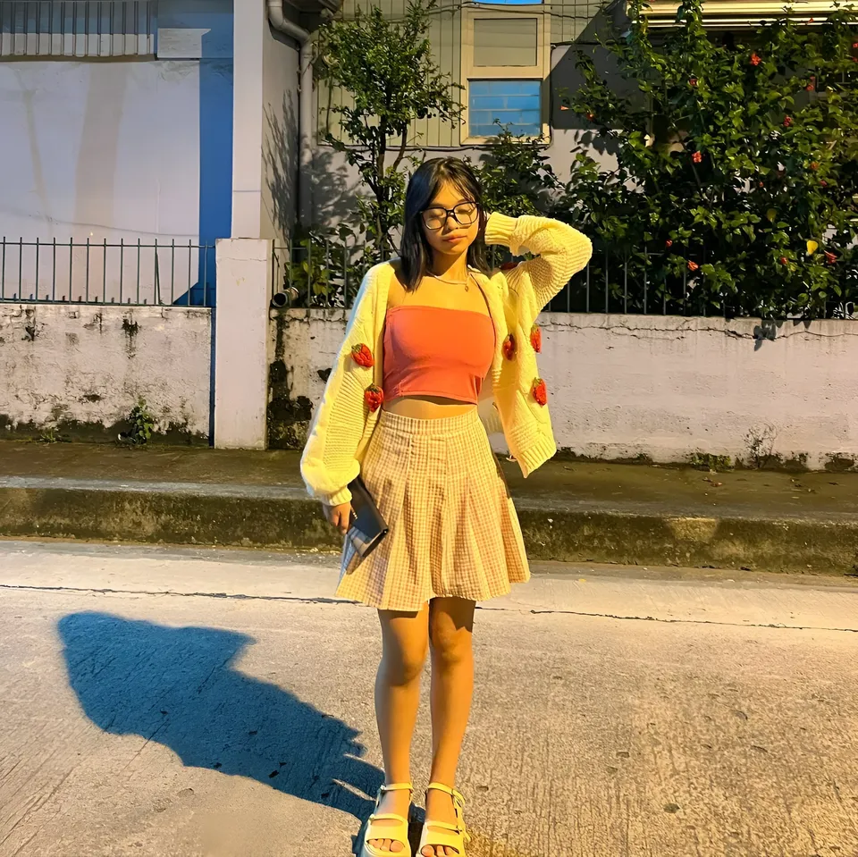 Beri Sinclair stands outdoors wearing yellow cardigan and orange top