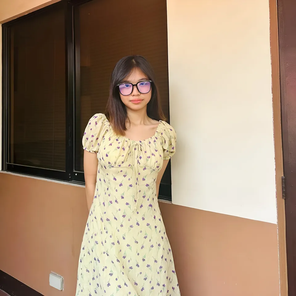 Beri Sinclair in yellow floral dress standing near window