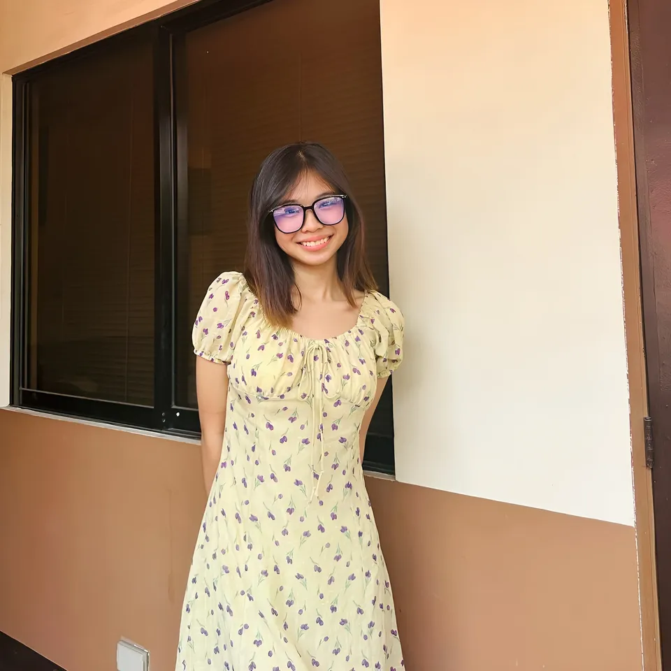Beri Sinclair in yellow floral dress standing near window