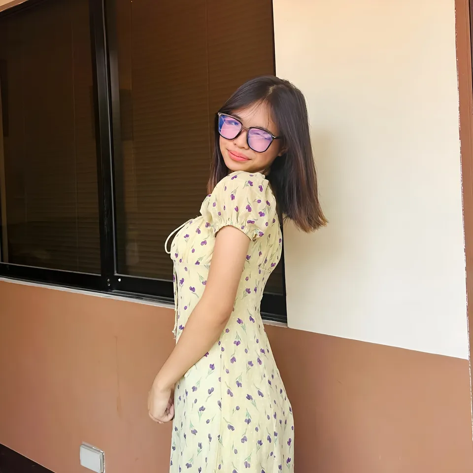 Beri Sinclair in yellow floral dress standing near window