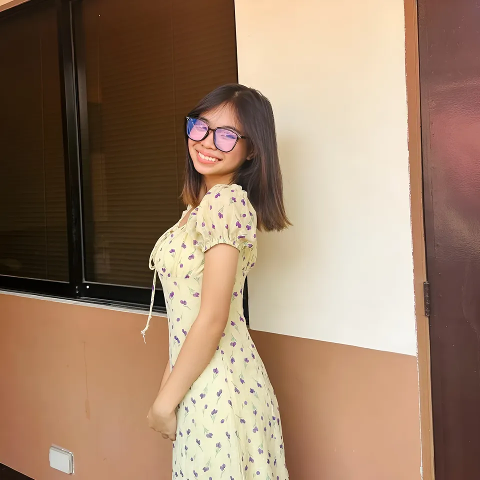 Beri Sinclair in yellow floral dress standing near window