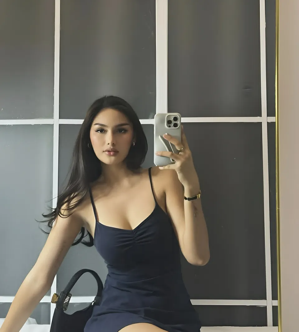 Brey Marti in dark blue dress taking mirror selfie with phone