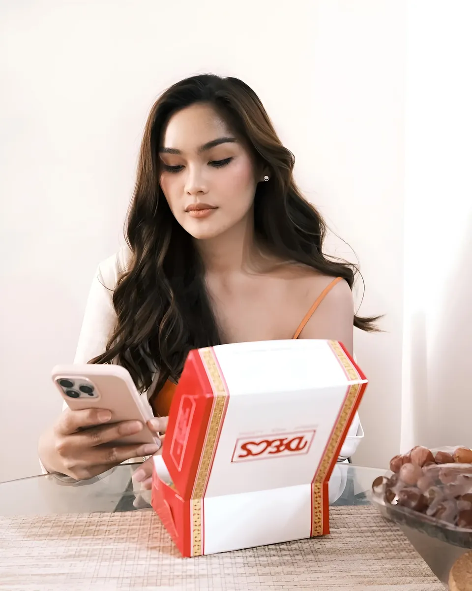 Brey Marti seated at table holding phone and red and white box