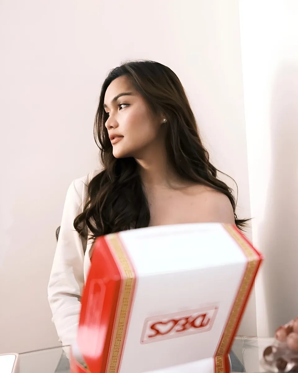 Brey Marti in white top holding red box, looking away