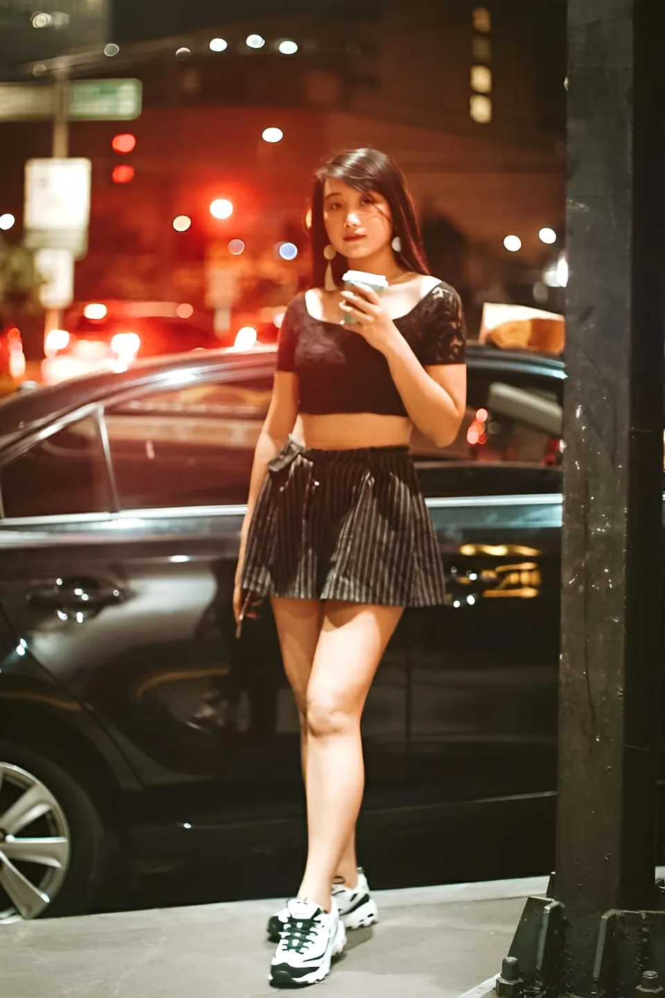 Camille Miguel Asuten in black crop top and striped skirt stands outdoors at night