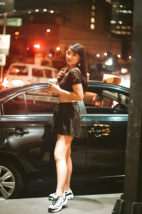 Camille Miguel Asuten wearing a black top and skirt stands beside a car at night
