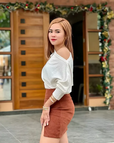 Cara Jade Atienza wearing a white top and brown skirt poses beside a doorway