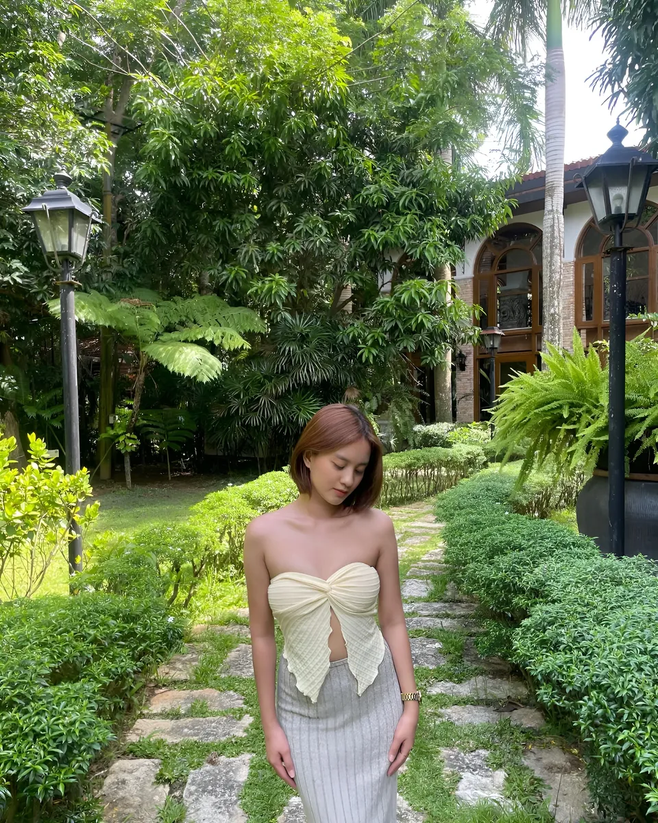Cassidy Rowan in beige top stands on stone path surrounded by greenery