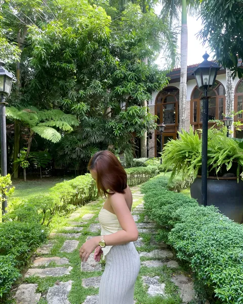 Cassidy Rowan in light-colored dress walks along stone path surrounded by greenery