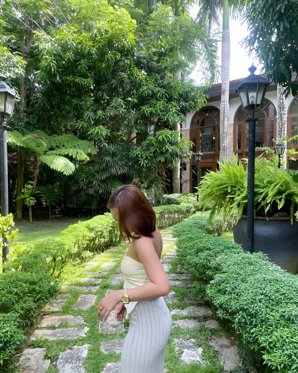 Cassidy Rowan in light-colored dress walks along stone path surrounded by greenery