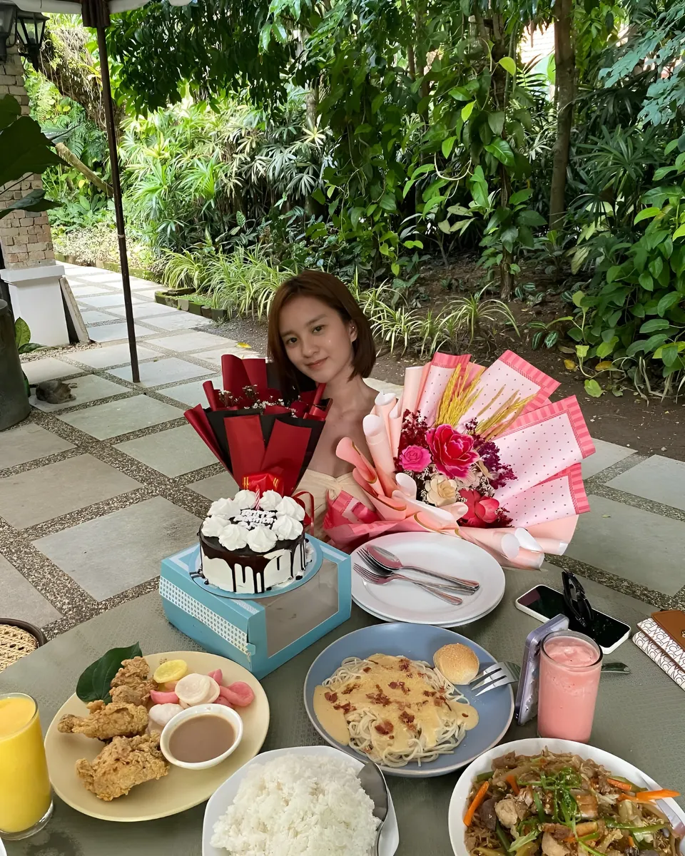 Cassidy Rowan seated at table with cake, flowers, and food outdoors