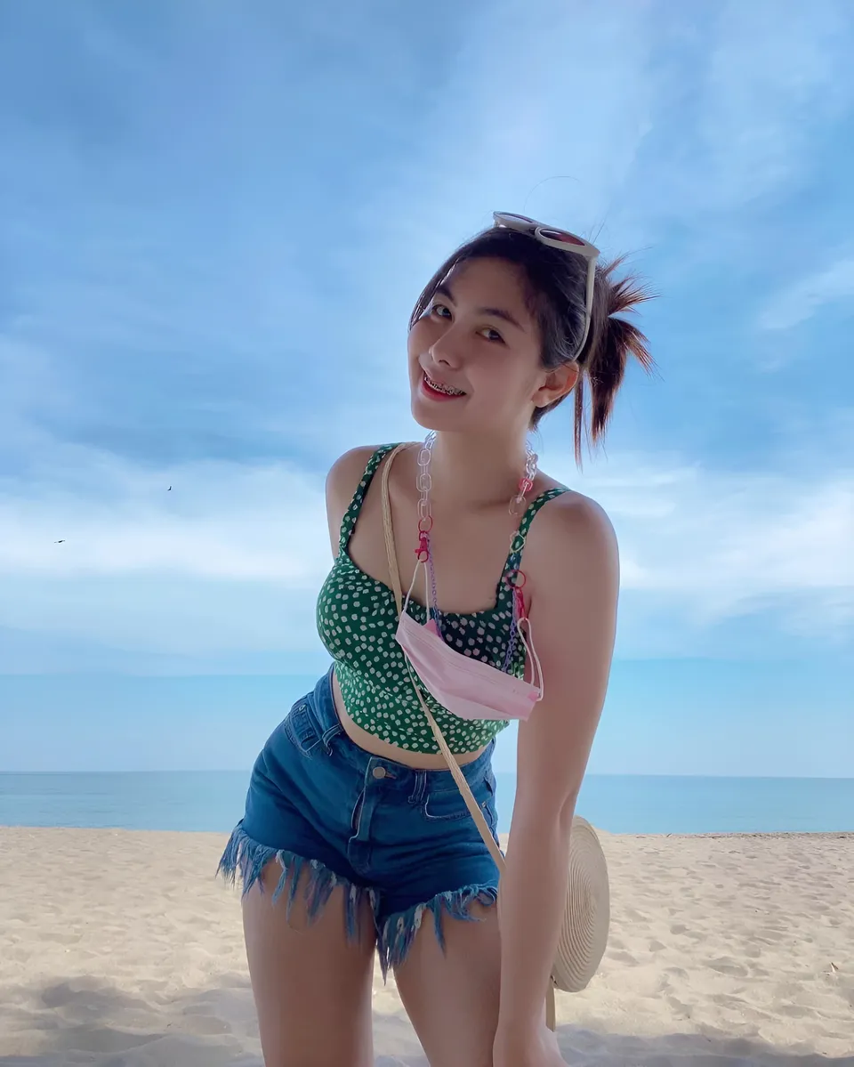 Cathy Holy wearing a patterned top and denim shorts poses on a sandy beach