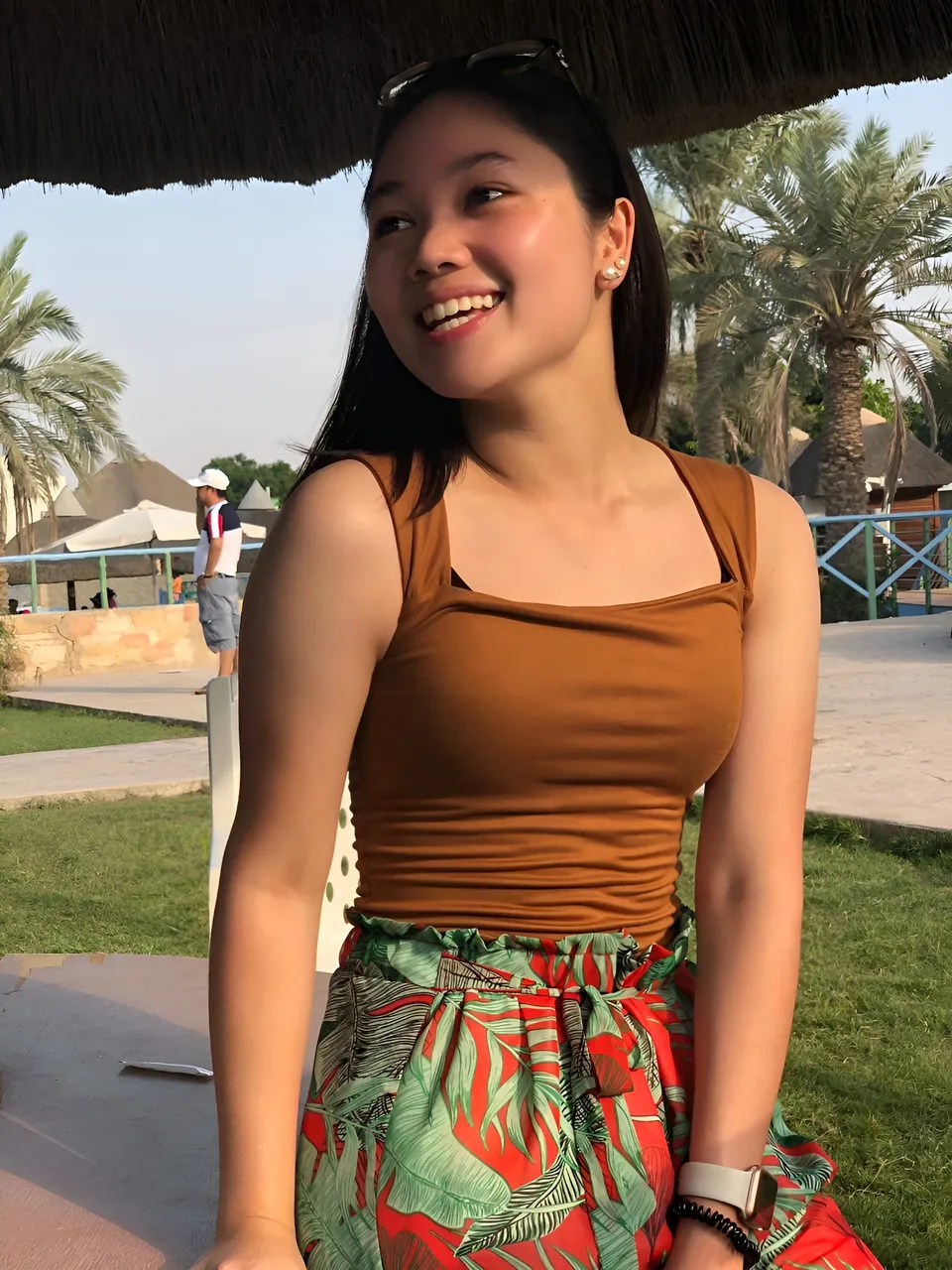 Chelle Avery in brown top and patterned pants sits under thatched roof