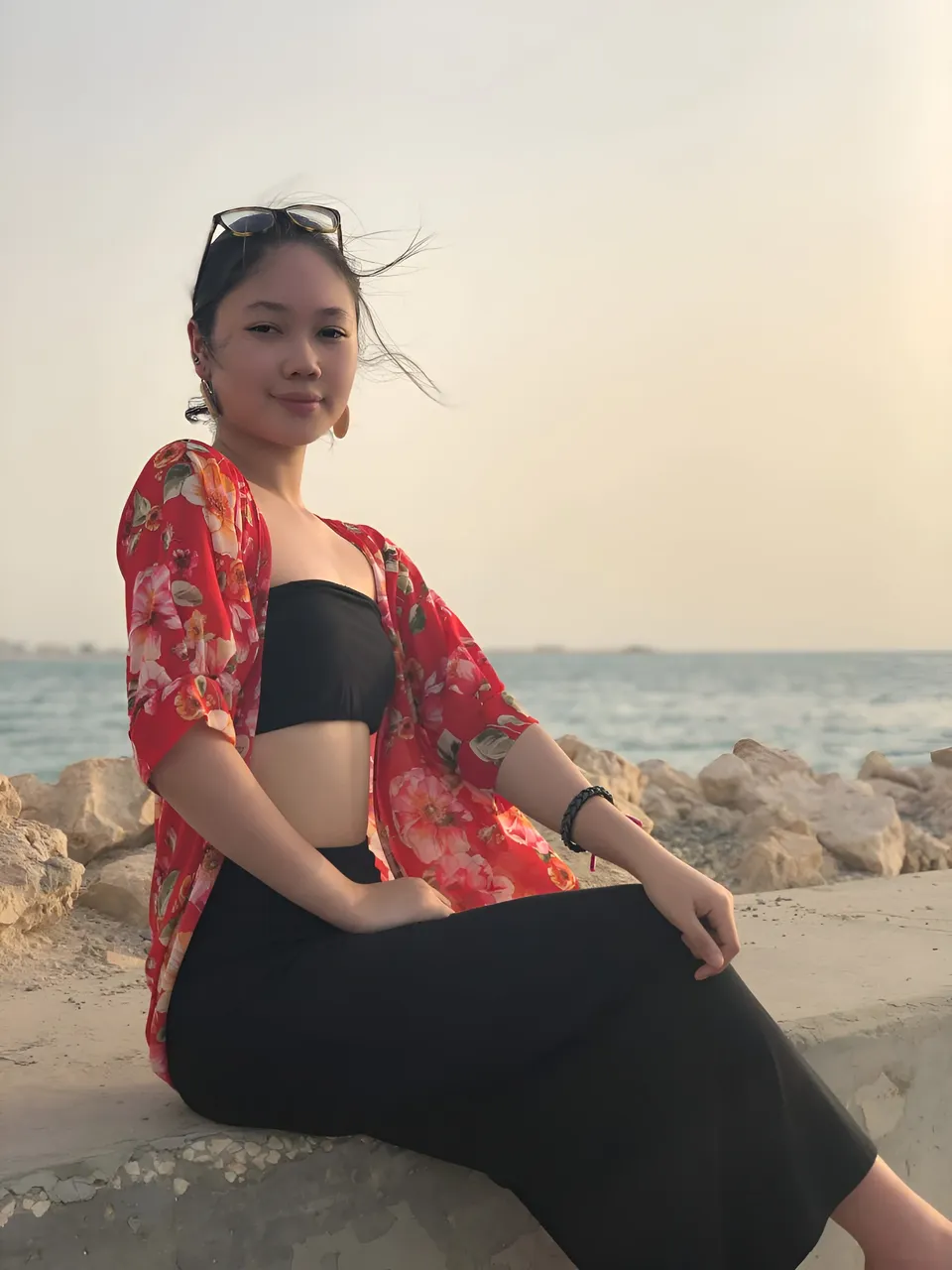 Chloe Arden in a red floral coverup and black outfit sits beside a rocky shoreline